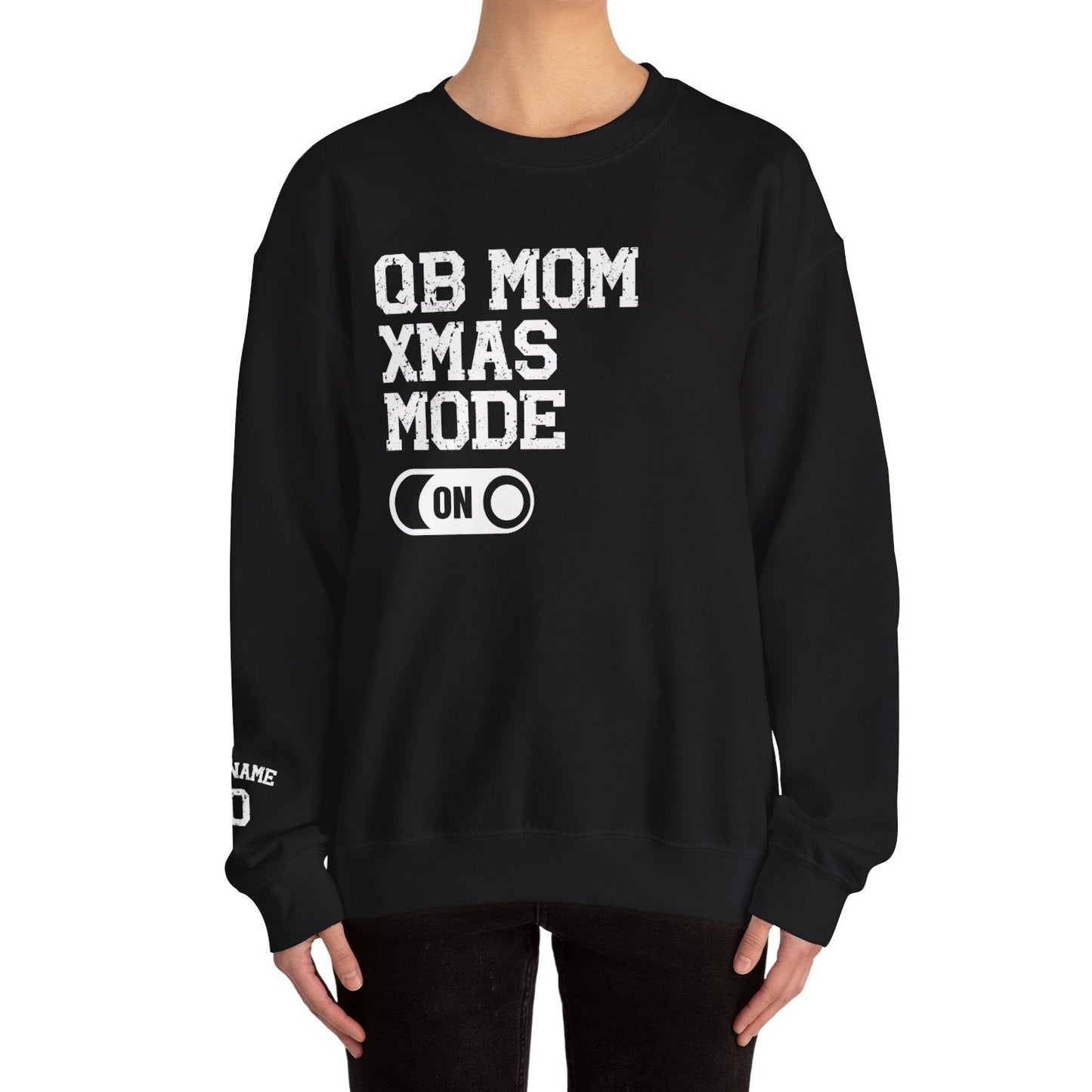 Black sweatshirt with 'QB MOM XMAS MODE ON' text worn by a person on a white background