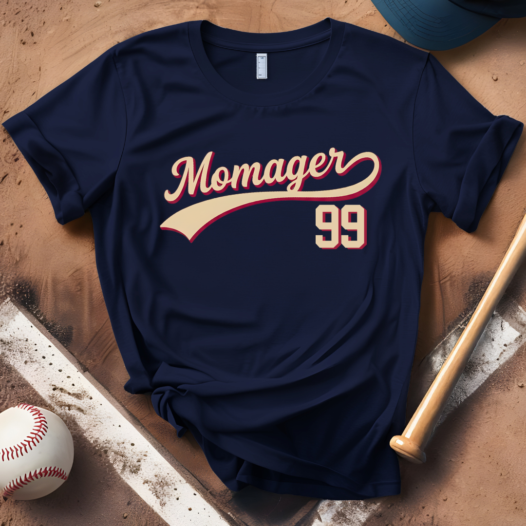 Navy blue t-shirt with 'Momager 99' text, placed on a wooden surface with a baseball and bat.